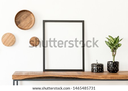 Stylish and cozy scandinavian interior of living room with wooden console, rings on the wall, plants and elegant accessories. Black mock up poster frame. Design home decor. Template. White walls.