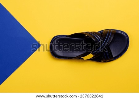 Stylish criss-cross black-blue men's slipper with embossing design isolated on a yellow-blue background with copy space. Fashion blogger content. Creative design for shoe store advertising poster.
