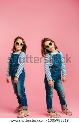 Stylish cute girls wearing fashion clothes. Girls posing in denim dungarees on pink background.
