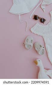 Stylish Cute Newborn Baby Summer Clothes, Accessories And Toys On Pastel Pink Background. Dress, Panama Hat, Shoes, Sunglasses. Neutral Pastel Pink Color. Flat Lay, Top View