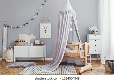 Stylish and cute scandinavian decor of  newborn baby room  with mock up poster , white design furnitures, natural toys, hanging grey canopy with wooden cradle, pillows, accessories and teddy bears. 