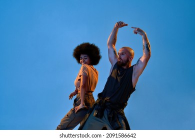 Stylish Dance Couple Dancing Breakdance. Concept Of Contemporary Dancing. Idea Of Choreography. Flexible Caucasian Man And Black Girl. Isolated On Blue Background In Studio. Copy Space