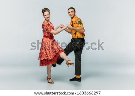 stylish dancers looking at camera while dancing boogie-woogie on grey background