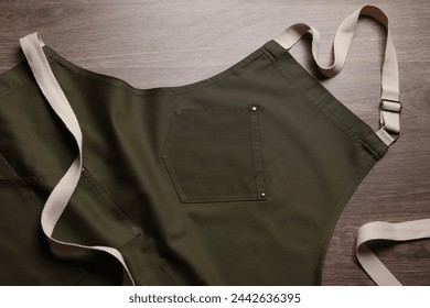 Stylish dark olive apron on wooden table, top view. Mockup for design