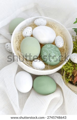 Stylish decorated easter eggs in a white bowl on linen cloth on a light wooden table. Happy Easter concept