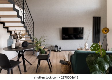 Stylish decorated living room with stairs, big tv screen, cozy sofa and small dining table