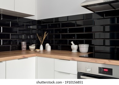 Stylish decoration on wooden countertops in small kitchen with black wall tiles