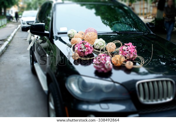 A stylish decoration of white\
flowers, ribbons and pink balls on a shiny bmw wedding\
car