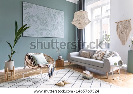 Stylish and design composition of living room with gray sofa, rattan armchair, cube, plaid, pillows, tropical plants, macrame and elegant accessories. Stylish home decor. Bright interior. Template.