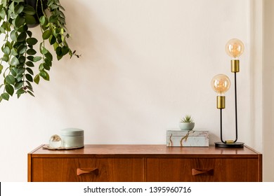 Stylish and design space of home interior with vintage cupboard, marble elegant accessories, hanging plant and gold table lamp. Cozy home decor. Minimalistic concept. Copy space. Real photo, Template.