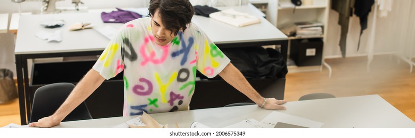 stylish designer standing near sewing patterns on desk in tailor shop, banner