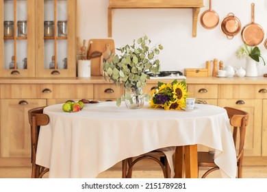Stylish dining room with wooden table and chairs. Cozy cuisine  decorated with summer decor and  table setting summer flowers and fruits. Holiday family dinner. kitchen interior with utensils, pans