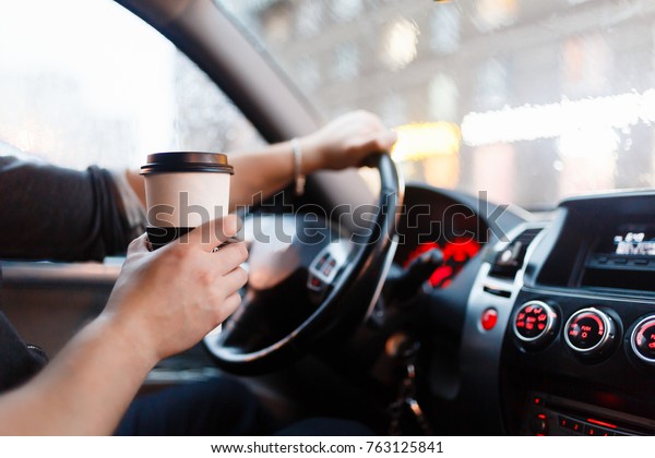 Stylish driver with a paper cup of hot coffee in\
hand in the driver\'s seat. The concept of inattention at the wheel,\
rest, coffee break to\
cheer.