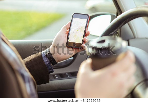 Stylish driver with a smart phone\
in hand and paper cup of hot coffee in the driver\'s seat. The\
concept of inattention at the wheel, rest, coffee break to\
cheer.