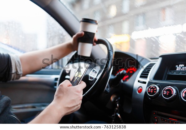 Stylish driver with a smartphone\
in hand and paper cup of hot coffee in the driver\'s seat. The\
concept of inattention at the wheel, rest, coffee break to\
cheer.