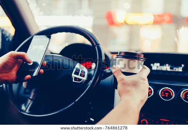 Stylish driver\
with a smartphone in hand and paper cup of hot coffee in the\
driver\'s seat. The concept of inattention at the wheel, rest,\
coffee break to cheer. Vintage style\
photo