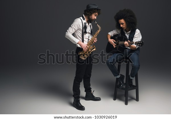 stylish duet of musicians playing sax and acoustic\
guitar on black