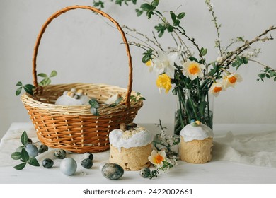 Stylish Easter bread, eggs and basket with food with spring flowers on rustic table. Happy Easter! Traditional easter holiday food. Modern natural dye eggs and daffodils and cherry blossom