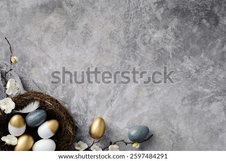 Stylish Easter eggs in a nest, surrounded by delicate white blossoms on a textured gray background. Happy Easter greeting card design.