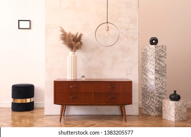 Stylish and eclectic interior of living room with design retro cabinet, round pendant lamp, marble pedestals and elegant accessories. Abstract background wall. Minimalistic home decor. Copy space. 
