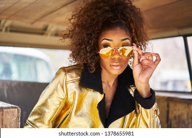 stylish edgy african american woman wearing golden jacket and sunglasses in old van