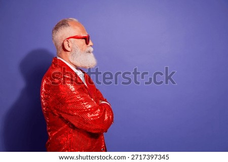 A stylish elderly man with a white beard wearing a bright red sequined jacket poses in profile beside a solid purple backdrop, conveying bold fashion, charisma, and festive energy suitable for advertising and entertainment themes.