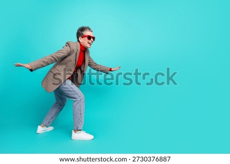 A stylish elderly model with short gray hair red glasses and casual chic outfit shows energy and fun in a bright teal studio setting