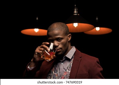 Stylish Elegant African American Man Drinking Whiskey In Dark Room With Lamps