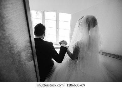 The stylish and elegant bridegroom and his pretty wife walking down the stairs holding hands - Shutterstock ID 1186635709