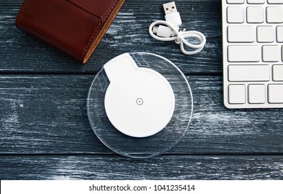 Stylish and elegant composition for business negotiations or website design. Wireless charging for the smartphone, keyboard, wallet, steel pen and glasses lie on a stylish vintage dark desk.