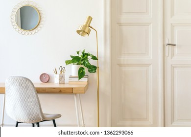 Stylish And Elegant Home Interior With Wooden Desk, Grey Velvet Chair, Design Accessories, Gold Lamp And Hanging Mirror On The White Wall. Piece Of Design Woman's Room. White Wooden Door. Copy Space. 