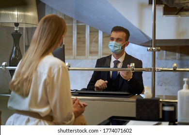 Stylish Elegant Man Sitting Behind The Glass Screen At The Reception Desk And Addressing The Woman In Front Of Him