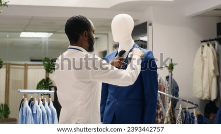Stylish employee arranging elegant clothes on mannequins in luxurious fashion boutique. Worker adding white pocket square to high street men blazer in fancy clothing store