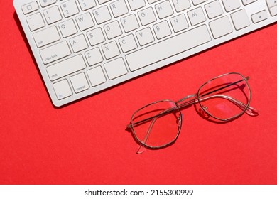 Stylish Eyeglasses And Computer Keyboard On Red Background