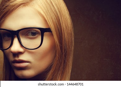 Stylish Eyewear Concept. Portrait Of A Young Beautiful Red-haired Model (student) Wearing Trendy Glasses And Posing Over Golden Background. Close Up. Copy-space. Studio Shot