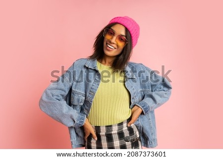 Stylish  fancy african woman in pink hat , cool sunglasses and  jeans jacket posing on pink background. Winter fashion look.