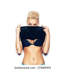 Stylish fashion blonde girl with tattoo in a black t-shirt showing his chest. Woman showing middle finger. White background, not isolated