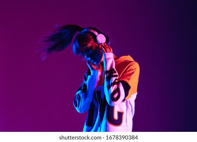 Stylish fashion teenager model wearing hoodie and headphones listening dj music dancing in purple neon lights. Young teen girl enjoy cool music 90s party mix in violet studio background. Copy space. - Shutterstock ID 1678390384