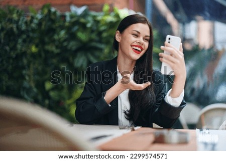 Stylish fashion woman blogger tourist sits in a cafe with a phone in her hands reads a message, mobile communication and internet on a journey, video call, freelance work online, smile with teeth