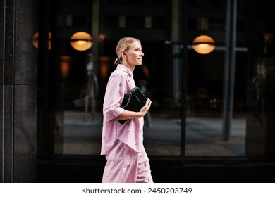 Stylish fashion woman in a pink suit, shirt and shorts walking confidently against a city backdrop. Urban street style allure.