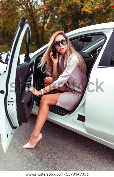 stylish fashionable beautiful Woman call on\
smartphone, enters from interior white car, business class sedan.\
Taxi, car sharing, summer city, sunglasses pink suit. parking lot,\
Long hair model.