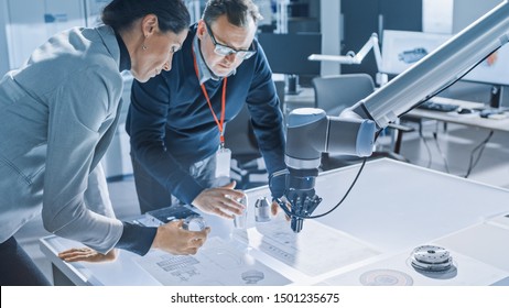 Stylish Female Engineer and Male Specialist Talking Lean on the Table Work with Blueprints, Documents and Tablet Computer. Working on Program and Manipulation of Robot Arm Movements. Modern Facility - Shutterstock ID 1501235675