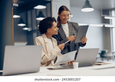 Stylish female executives managers discussing financial accounting papers and using digital tablet  - Powered by Shutterstock