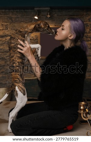 Stylish female model posing affectionately with brindle whippet in loft