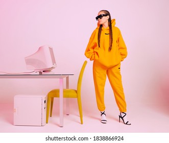 Stylish Female Office Worker In Sunglasses And Hoodie Standing With Obsolete Computer. Colored Neon Light