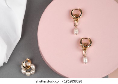 Stylish female ring earrings with pearls on trendy pink podium, gray background, top view. High quality photo