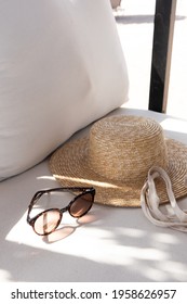 Stylish female sunglasses, straw hat, shopper bag on white lounge couch with pillows. Women's fashion beach accessories for summer travel, vacation. Fashion blog, magazine, social media. 