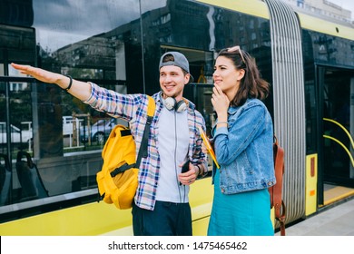 Stylish Female Traveler With Backpack And Smartphone In Hand Asking For Help Man With Backpack At Tram Stop. Young Woman Tourist Asking For Directions And Help From Local People In Tram Stop Outdoor.