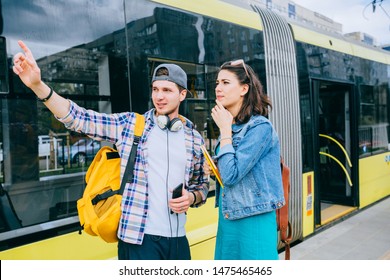 Stylish Female Traveler With Backpack And Smartphone In Hand Asking For Help Man With Backpack At Tram Stop. Young Woman Tourist Asking For Directions And Help From Local People In Tram Stop Outdoor.