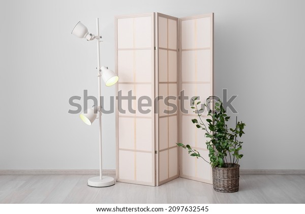 Stylish folding screen with lamp and houseplant\
in room interior